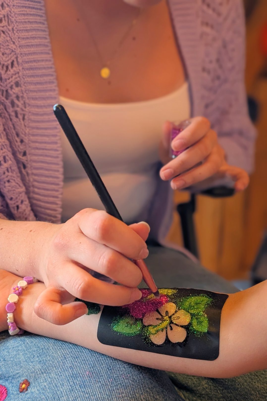Detailaufnahme Kinderschminkerin trägt Glitzertattoo auf Kinderhand auf